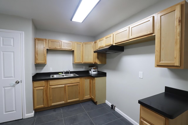 kitchen with light brown cabinetry, a sink, dark countertops, baseboards, and dark tile patterned flooring