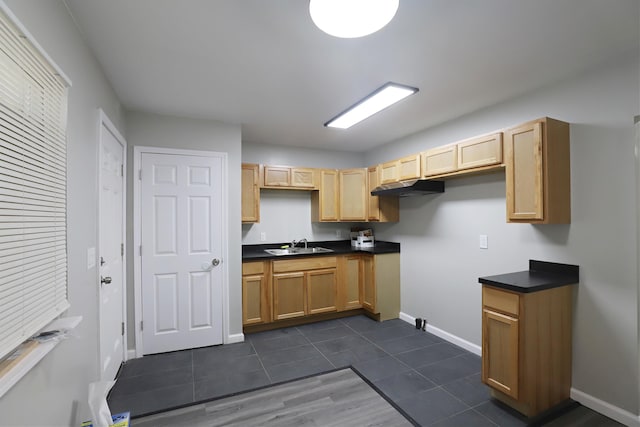 kitchen with dark countertops, light brown cabinets, a sink, dark tile patterned floors, and baseboards