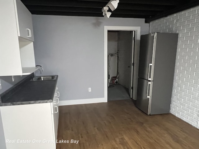 8311 Goldfinch Rd, Freeland, MI 48623 - kitchen with freestanding refrigerator, wood finished floors, white cabinetry, brick wall, and beam ceiling