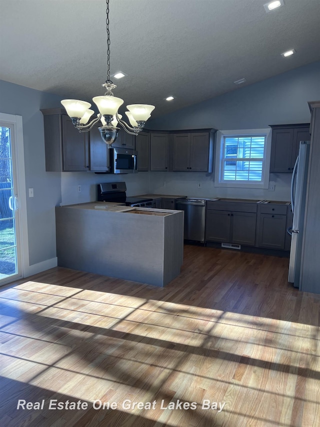 8311 Goldfinch Rd, Freeland, MI 48623 - kitchen featuring appliances with stainless steel finishes, a chandelier, dark wood-style flooring, lofted ceiling, and a peninsula