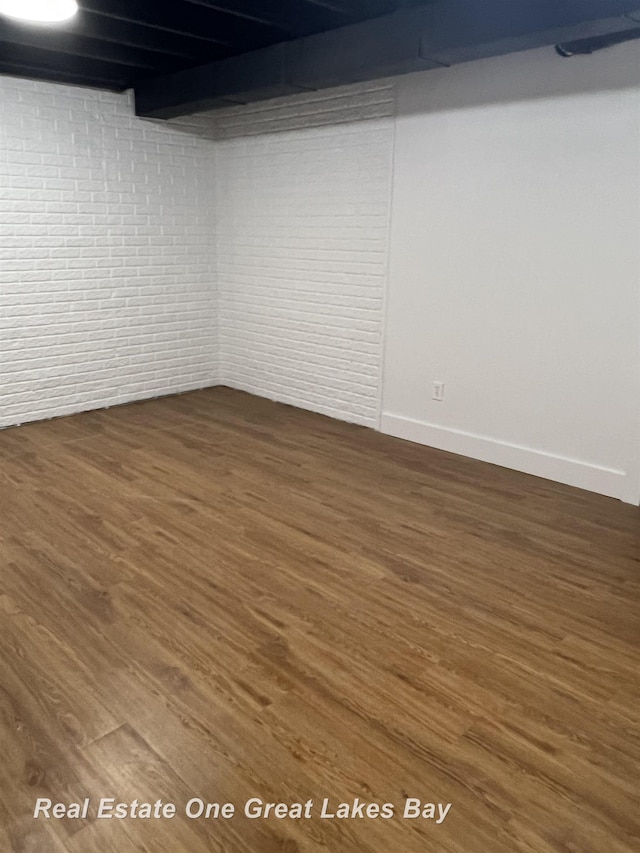 finished basement featuring dark wood-type flooring, baseboards, and brick wall