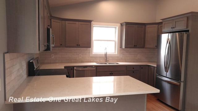 8311 Goldfinch Rd, Freeland, MI 48623 - kitchen featuring stainless steel appliances, lofted ceiling, tasteful backsplash, a peninsula, and light wood-type flooring