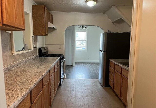327 E Main St, Vermontville, MI 49096 - kitchen featuring brown cabinetry, arched walkways, light wood-style floors, and appliances with stainless steel finishes