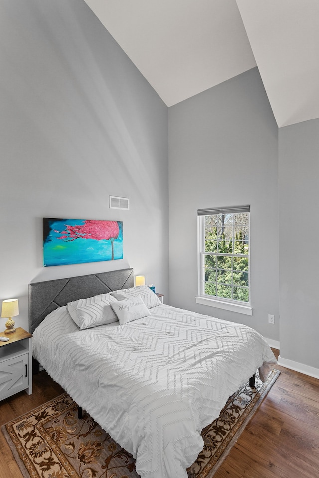 bedroom with lofted ceiling, wood finished floors, visible vents, and baseboards
