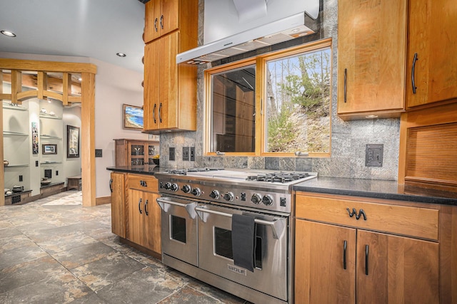 kitchen featuring dark countertops, extractor fan, brown cabinetry, backsplash, and range with two ovens