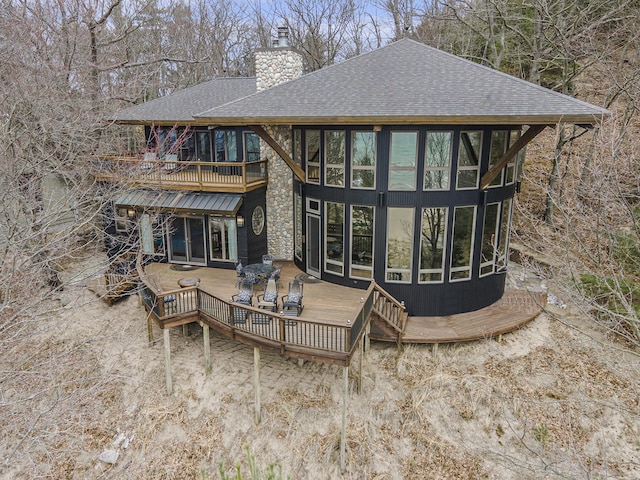 back of house with a chimney, a wooden deck, roof with shingles, and a balcony