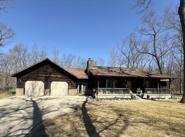 view of front facade with a chimney, driveway, an attached garage, brick siding, and covered porch