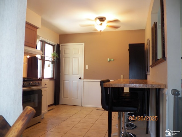 7303 Cranbrook Dr, Lambertville, MI 48144 - kitchen with stainless steel gas range oven, a wainscoted wall, a ceiling fan, light tile patterned floors, and under cabinet range hood