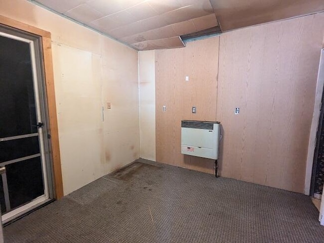 carpeted empty room featuring heating unit and wooden walls