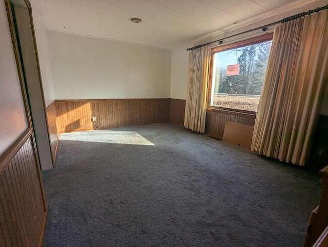 carpeted empty room featuring visible vents, a wainscoted wall, and wooden walls