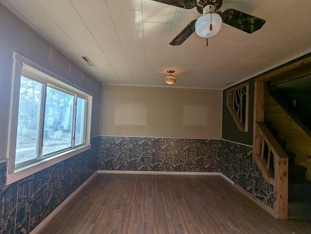 empty room featuring wallpapered walls, wood finished floors, a ceiling fan, baseboards, and wainscoting