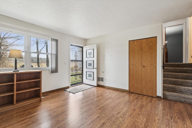 interior space featuring a textured ceiling, visible vents, stairway, wood finished floors, and baseboards