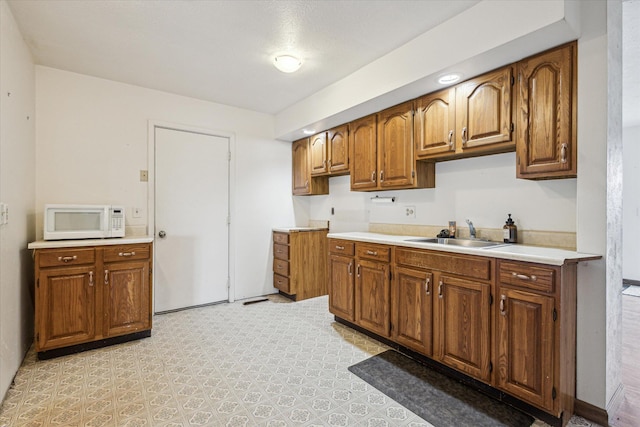 kitchen with light countertops, white microwave, brown cabinets, and a sink