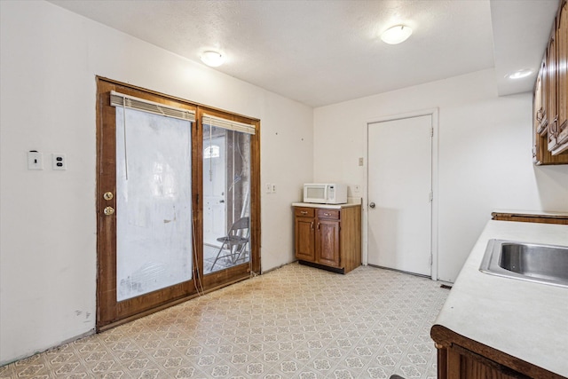 interior space featuring white microwave, light floors, brown cabinetry, a sink, and light countertops