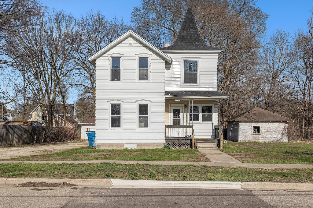 view of front of home with a porch, a shingled roof, an outbuilding, and a front lawn