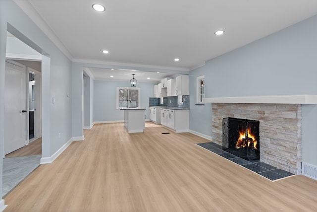 19319 Pennington Dr, Detroit, MI 48221 - unfurnished living room featuring a sink, baseboards, recessed lighting, light wood-style floors, and a stone fireplace