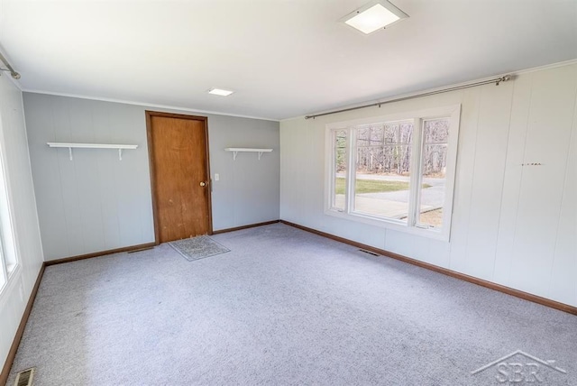 carpeted spare room featuring baseboards, visible vents, and crown molding