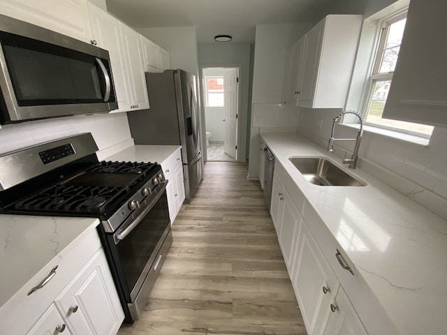 kitchen featuring light wood-style flooring, a sink, white cabinetry, light stone countertops, and appliances with stainless steel finishes