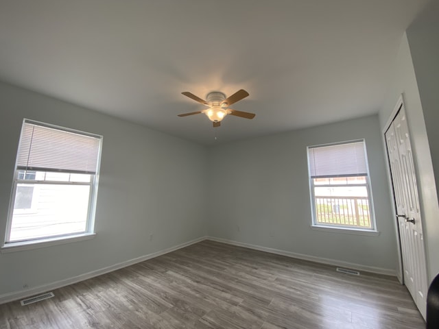 spare room with baseboards, a ceiling fan, wood finished floors, and visible vents