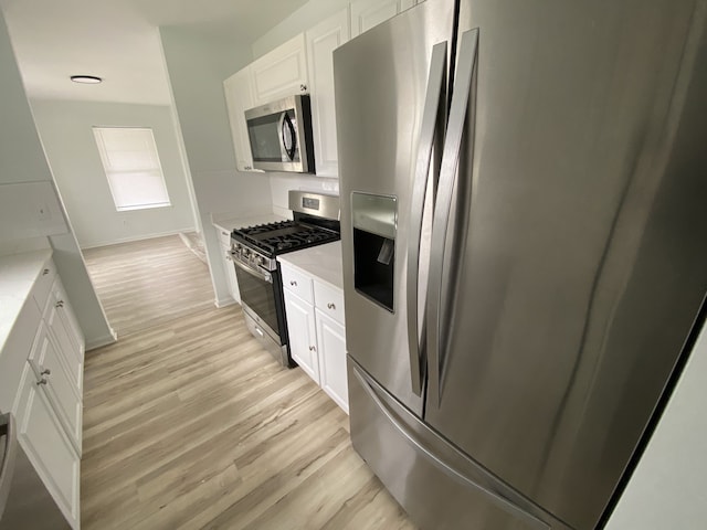 kitchen with light wood finished floors, stainless steel appliances, white cabinets, baseboards, and light stone counters