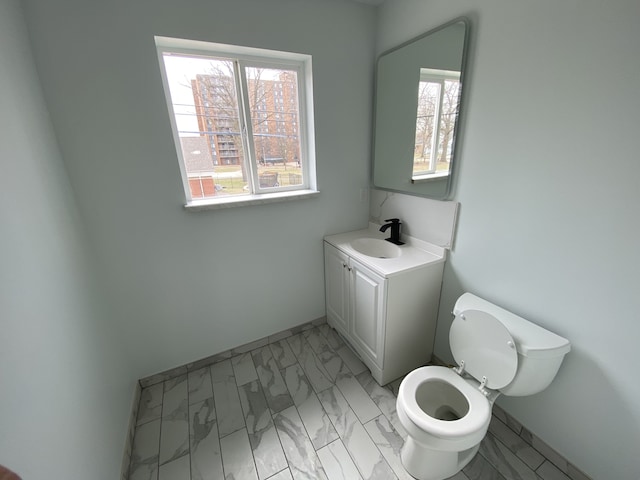 half bath with a wealth of natural light, marble finish floor, vanity, and toilet