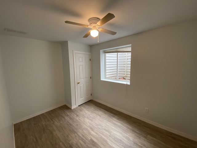 spare room with wood finished floors, a ceiling fan, and baseboards