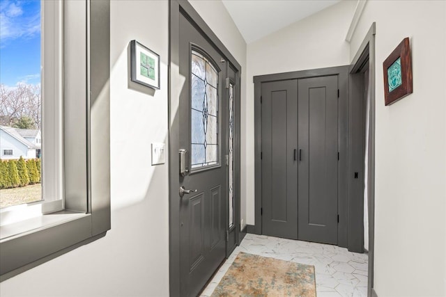 doorway with vaulted ceiling and marble finish floor