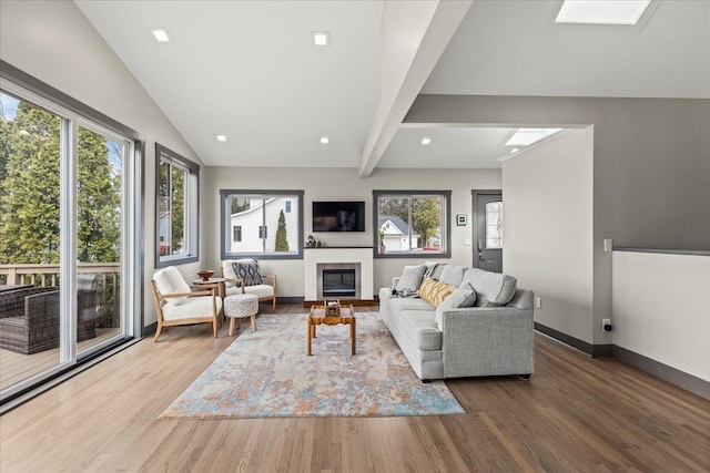 living room featuring wood finished floors, lofted ceiling with skylight, a glass covered fireplace, baseboards, and recessed lighting