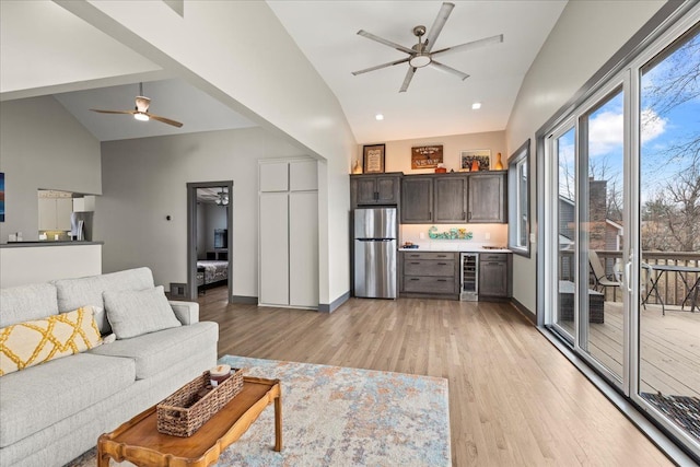 living area featuring ceiling fan, beverage cooler, a bar, and light wood-style flooring