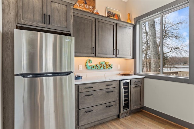 kitchen with baseboards, light wood-type flooring, wine cooler, and freestanding refrigerator