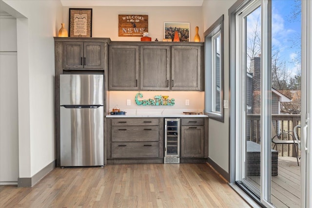 bar with baseboards, light wood-type flooring, wine cooler, and freestanding refrigerator