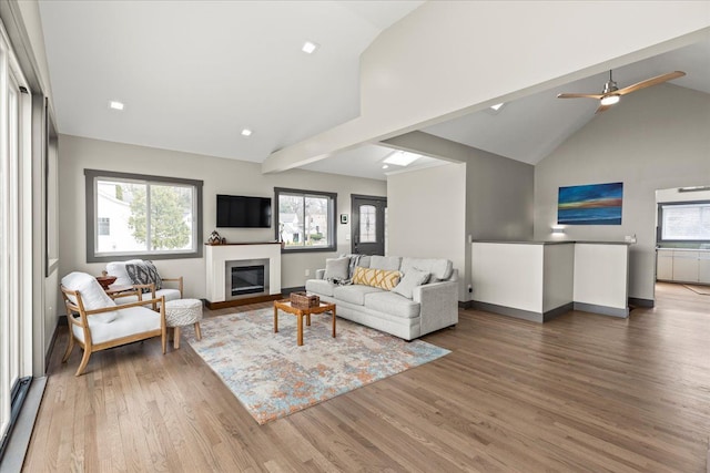 living room with a glass covered fireplace, a ceiling fan, wood finished floors, and high vaulted ceiling