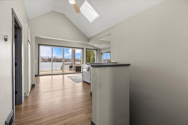 hallway featuring wood finished floors, a water view, a skylight, and high vaulted ceiling