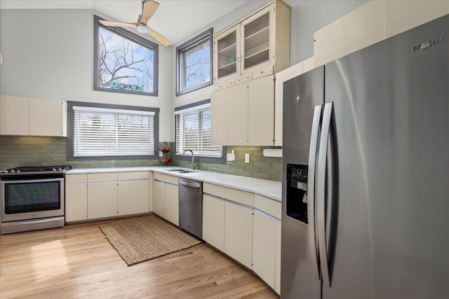 kitchen featuring light countertops, a sink, light wood-type flooring, decorative backsplash, and appliances with stainless steel finishes
