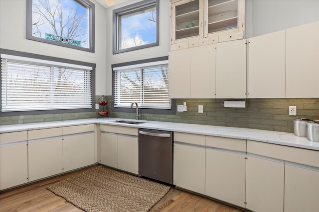kitchen with dishwasher, a sink, light wood-style flooring, and tasteful backsplash