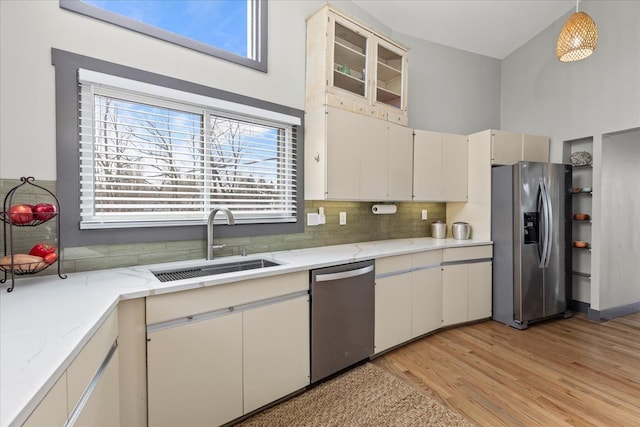 kitchen with stainless steel appliances, light wood-style flooring, a sink, decorative backsplash, and light stone counters