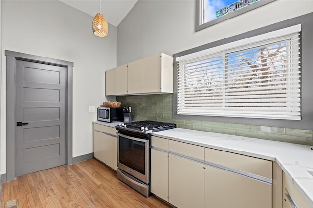 kitchen featuring light wood-style flooring, visible vents, decorative backsplash, high vaulted ceiling, and appliances with stainless steel finishes