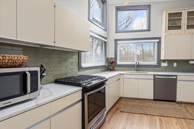 kitchen featuring tasteful backsplash, a sink, light wood finished floors, appliances with stainless steel finishes, and light stone countertops