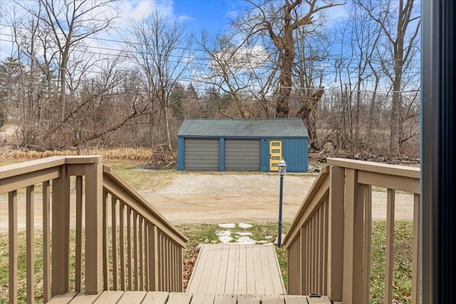 wooden terrace featuring dirt driveway, a detached garage, and an outbuilding