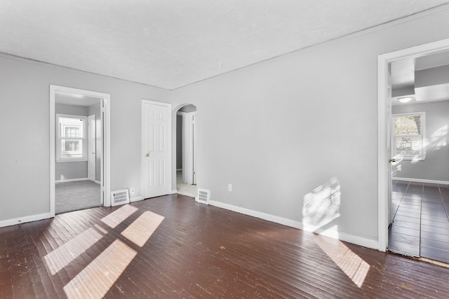 unfurnished bedroom with arched walkways, wood-type flooring, baseboards, and multiple windows