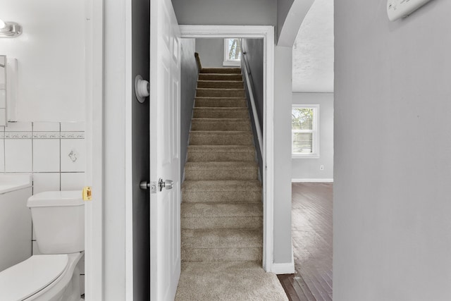stairs featuring baseboards, wood finished floors, and arched walkways