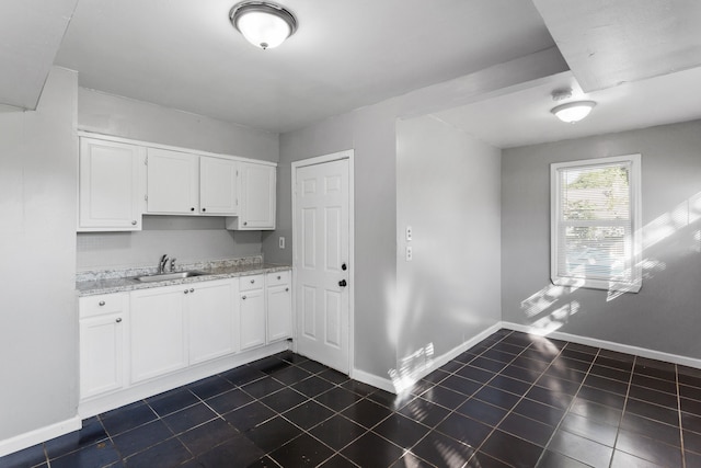 kitchen featuring a sink, dark tile patterned flooring, white cabinets, baseboards, and light stone countertops