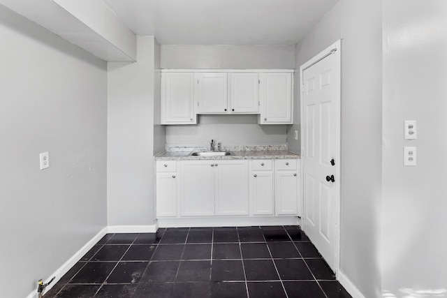 laundry room with baseboards, a sink, and dark tile patterned flooring