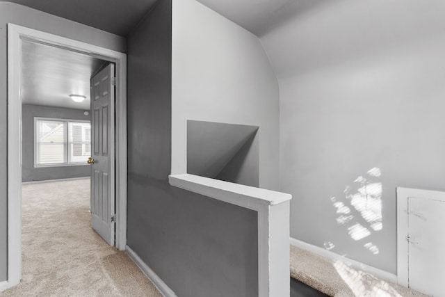 hall featuring carpet flooring, baseboards, and an upstairs landing