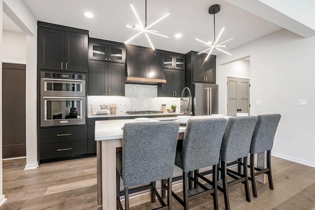 2359 Elinor Ln SE, East Grand Rapids, MI 49506 - kitchen featuring decorative backsplash, an island with sink, stainless steel appliances, light countertops, and custom range hood