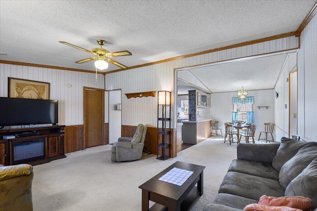 carpeted living room with crown molding, a textured ceiling, wallpapered walls, ceiling fan with notable chandelier, and wainscoting