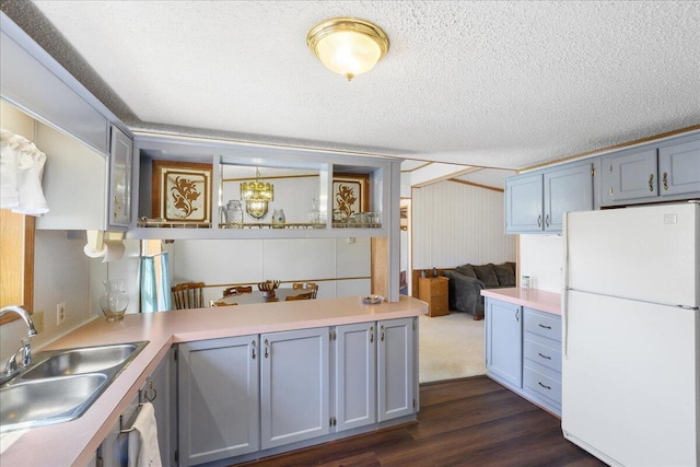 kitchen featuring a sink, light countertops, a peninsula, dark wood-style flooring, and freestanding refrigerator