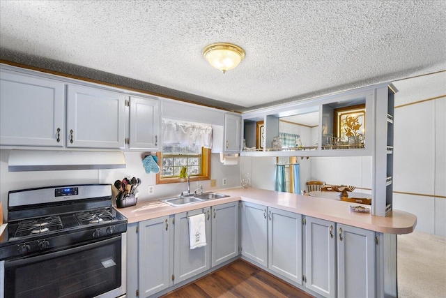 kitchen featuring a sink, light countertops, gas range oven, a peninsula, and under cabinet range hood