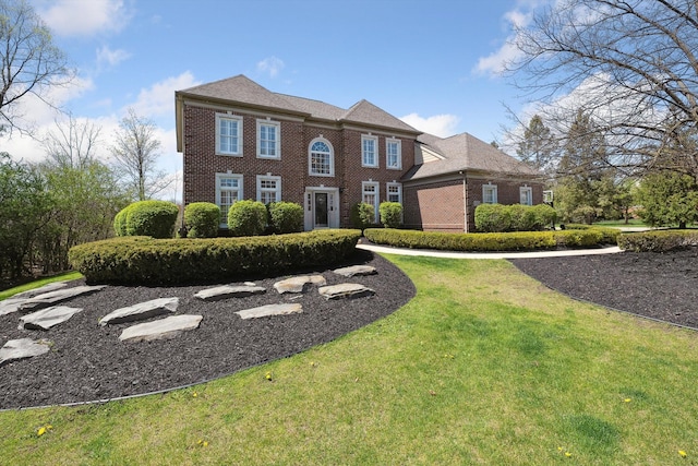 colonial inspired home featuring brick siding and a front yard