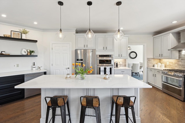 kitchen with wall chimney range hood, appliances with stainless steel finishes, a breakfast bar, and dark wood finished floors